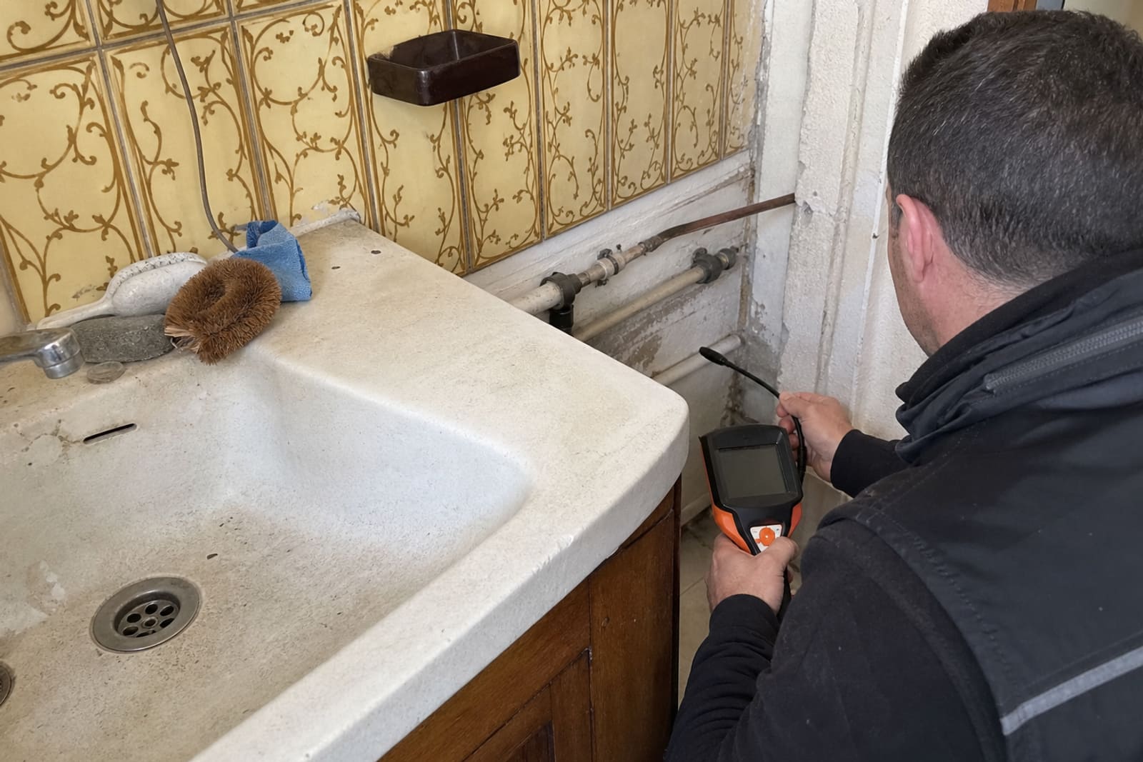 technicien inspecte canalisation apparente dans cuisine ancienne